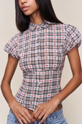 A woman wearing a short-sleeve collared button-up shirt with a red, white, and gray plaid pattern and small embroidered motifs, paired with blue jeans.